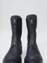 Botas de cuero color marrón de caña alta, con plataforma gruesa de goma y cierre metálico frontal con tirador. Presentan costuras a contratono y detalle de etiqueta de la marca en la lengüeta.