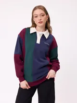 Sweater estilo rugby de Rusty, con diseño color block en tonos bordó, azul marino y verde. Presenta cuello polo en color crema con cierre frontal de botones, mangas largas con puños elásticos y logo de la marca bordado en el pecho.