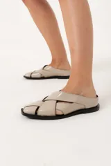 Zuecos color hueso con diseño de tiras cruzadas y suela plana color negro.