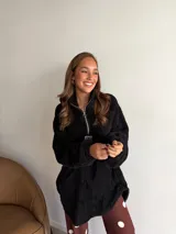 Buzo de corderito negro con cuello alto y cierre frontal parcial. Presenta un diseño holgado de manga larga con textura suave y abrigada.