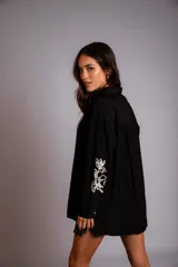 Camisa beige de corte amplio, con cuello clásico, cierre frontal con botones, mangas largas con puños abotonados y bordado floral en las mangas.