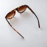 Lentes de sol tipo aviador con armazón negro de policarbonato y detalles metálicos dorados en las patillas. Lentes oscuros con filtro UV400.