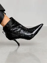 Botín de cuero negro con acabado charol, diseño de punta fina y taco aguja. Cuenta con cierre posterior y una silueta elegante.