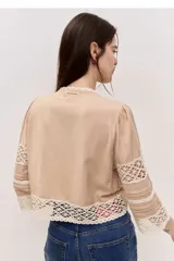 Blusa tostada con mangas tres cuartos, detalles de encaje floral calado y cierre frontal con lazos.