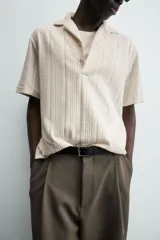 Polo de hombre color crema, de tejido texturado con rayas verticales en relieve, corte relajado, cuello bowling y cierre frontal parcial con botones.