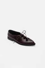 Zapato acordonado de cuero color bordó, con punta fina y diseño estilo oxford. Presenta cordones al tono y detalles de ojales metálicos dorados.