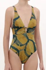 Malla enteriza estampada en tonos mostaza y verde oscuro, con escote en V profundo y detalle de argolla metálica en el centro del pecho.