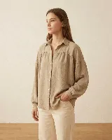 Camisa de calce amplio color beige, con cuello camisero, hombros caídos y mangas largas con puño elastizado. Presenta detalle de frunce en el delantero y la espalda, con cierre frontal de botones.
