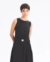 Vestido largo negro sin mangas, con cuello redondo, corte holgado y abertura lateral en la falda. Presenta un cinturón con hebilla metálica plateada.