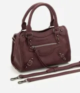 Cartera satchel Satinato de color negro, confeccionada en poliuretano. Cuenta con asas de mano fijas, correa larga removible, bolsillos frontales con cierre, tachas metálicas decorativas y tiras colgantes.