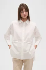 Camisa blanca de algodón, holgada, con cuello camisero, cierre frontal con botones y mangas largas.