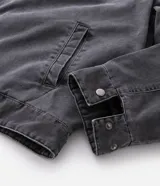 Chaqueta de denim color gris con acabado estonado, cierre frontal con cremallera, cuello camisero y manga larga. Presenta un estampado con la palabra 'OUTLAW' en tipografía gótica en el pecho y un bolsillo con cierre en la manga izquierda.