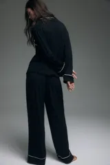 Pijama de dos piezas negro, compuesto por una camisa de manga larga con solapas de muesca, ribetes blancos y cierre de botones, y un pantalón de pierna ancha con elástico revestido en la cintura y ribetes blancos en los puños.