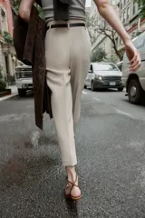 Pantalón de tiro alto y corte tobillero, confeccionado en tejido de aspecto denim oscuro. Presenta diseño de pinzas frontales, bolsillos laterales y cierre frontal con cremallera, botón y gancho. Incluye un cinturón fino a tono con hebilla metálica dorada.