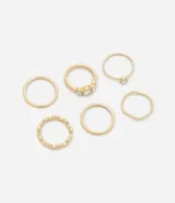 Set de seis anillos de metal en tono dorado con diseños variados, incluyendo modelos lisos, texturizados y con incrustaciones de piedras brillantes.