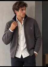 Campera de tejido gris con cierre frontal completo, cuello alto y puños y cintura de canalé. Cuenta con un pequeño bordado en el pecho.
