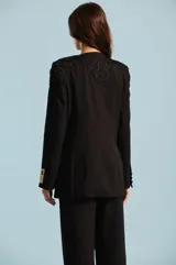 Saco sastre negro con detalles de bordados y pedrería en los hombros y solapas, de manga larga con etiqueta decorativa en el puño y cierre frontal de un botón.