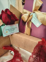Caja de regalo artesanal color bordó con moño dorado, diseñada como experiencia de lujo para presentar un conjunto de lencería. Incluye elementos de regalo adicionales como perfume, rosa natural y dulces.