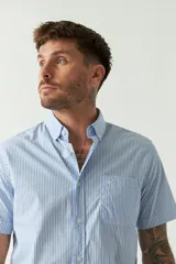 Camisa de manga corta con estampado de cuadros vichy en azul y blanco. Presenta cuello con botones, cierre frontal con botones y logo bordado en el pecho.