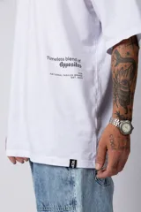Remera blanca de corte oversize con cuello redondo y mangas cortas. Presenta un pequeño estampado tipográfico en la parte inferior frontal y un diseño gráfico de mayor tamaño en la espalda.