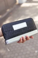 Billetera mediana de cuero negro con textura croco y detalles plateados. Tiene cierre y logo de la marca en el frente.