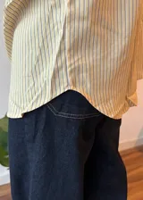 Camisa oversize de corte amplio con estampado de rayas verticales finas en tonos amarillo y azul. Presenta cuello clásico, cierre frontal con botones, mangas largas con puños abotonados y un bolsillo en el pecho.