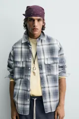 Camisa de algodón de corte relajado, con cuello solapa, manga larga terminada en puño con botón y dos bolsillos de plastrón con solapa en el pecho. Presenta un estampado de cuadros en tonos azules, grises y blancos, y cierre frontal de botonadura.