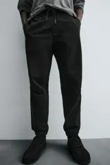 Pantalón tipo jogger de corte slim fit, confeccionado en tejido de algodón con elasticidad. Presenta cintura elástica ajustable con cordón, bolsillos frontales, bolsillos traseros de vivo y bajos con puños elásticos.