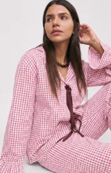 Conjunto de dos piezas de pijama confeccionado en algodón a cuadros vichy rosados y blancos. Incluye una camisa de manga larga con puños acampanados y cierre delantero con cordones para atar, y un pantalón largo de corte recto con volados en el ruedo.