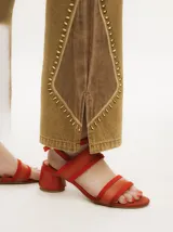 Pantalón de denim color tostado con tiro alto y corte oxford. Presenta detalles de apliques metalizados a lo largo de las costuras laterales y en los bolsillos.