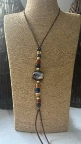 Collar largo de estilo artesanal con cordón de cuero marrón y una serie de cuentas de piedra natural y metal dorado dispuestas verticalmente.