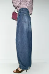 Jeans de tiro alto con diseño barrel, caracterizado por una silueta curvada y holgada en la zona de los muslos y rodillas, estrechándose hacia el tobillo. Cuenta con cinco bolsillos y cierre frontal con cremallera y botón.