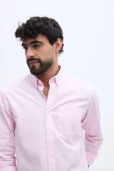 Camisa de manga larga color rosado, con cuello abotonado, cierre frontal de botones y un bolsillo ojal en el pecho.