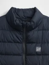 Chaleco puffer acolchado de color beige, con cierre frontal de cremallera, cuello alto y logo de la marca bordado en el pecho.