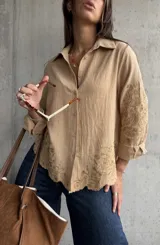 Camisa de lino color camel con cuello clásico, cierre frontal de botones y mangas largas. Presenta un delicado bordado floral tono sobre tono en las mangas y en el ruedo, el cual tiene un acabado festoneado.