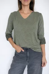 Sweater de punto color verde oliva con escote en V y mangas largas. Presenta un diseño liso en el exterior y un detalle de animal print en el interior de los puños, visible al doblarlos.