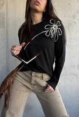 Remera de manga larga color negro, de corte recto, con aplique decorativo en relieve con forma de flor grande en el hombro confeccionado con cordón trenzado en blanco y negro.