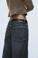 Jeans de tiro medio con diseño baggy barrel, confeccionados en denim color beige con efecto lavado. Presentan cinco bolsillos, costuras laterales torcidas y cierre frontal con cremallera y botón metálico.