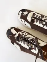 Zapatilla deportiva de cuero con estampado de vaca (pelo), color marrón y blanco. Suela blanca gruesa.