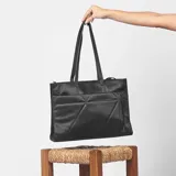 Bolso negro tipo tote bag con diseño geométrico acolchado en el frente y cierre superior. Tiene doble asa de hombro y correa bandolera extraíble.
