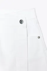 Falda pantalón corta de tiro alto color blanco, con bolsillos delanteros y traseros. Cierre frontal cruzado con cremallera oculta y botón metálico.