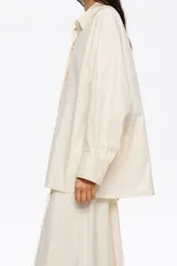 Camisa oversize de algodón color celeste, con cuello camisero, botones frontales y mangas largas ranglán con puños abotonados. Presenta pespuntes a contraste en toda la prenda.