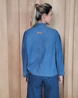 Camisa de denim con cuello alto tipo mao con volados, cierre frontal con botones y mangas largas con puños elásticos con volados.