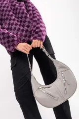 Bandolera gris claro en forma de media luna con dos cierres plateados en el frente y correa ajustable.