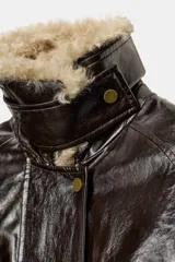 Chaqueta de efecto cuero color marrón oscuro con acabado brillante, cuello de solapa con aplicación de pelo sintético extraíble, manga larga con trabillas, bolsillos frontales de plastrón con solapa y cierre frontal con cremallera y botones a presión.