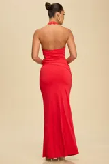 Vestido largo de fiesta color rojo, con cuello halter y diseño ajustado al cuerpo. Presenta una abertura lateral en la cintura con detalle de argollas metálicas.