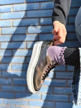 Zapatillas deportivas de cuero color peltre, con cordones negros y suela de goma blanca.