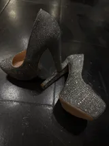 Zapatos de tacón alto tipo plataforma, color negro, completamente cubiertos de pedrería brillante. Presentan un taco grueso y una plataforma delantera que aporta altura y estabilidad.