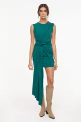 Vestido corto sin mangas de color verde oscuro, con diseño drapeado, nudo en la cintura y una larga caída de tela asimétrica en el lateral delantero.
