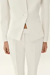 Blazer entallado color blanco de cuello sin solapa, manga larga con hombreras, falsos bolsillos delanteros de vivo y cierre frontal con un botón.